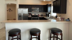 A modern kitchen with dark cabinets, stainless steel appliances, and a bar area with stools.