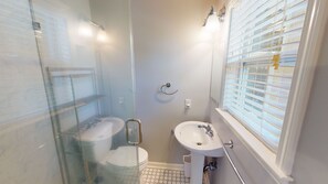 Ein Badezimmer mit einer Duschkabine, Toilette, Waschbecken und einem Fenster mit Jalousien.