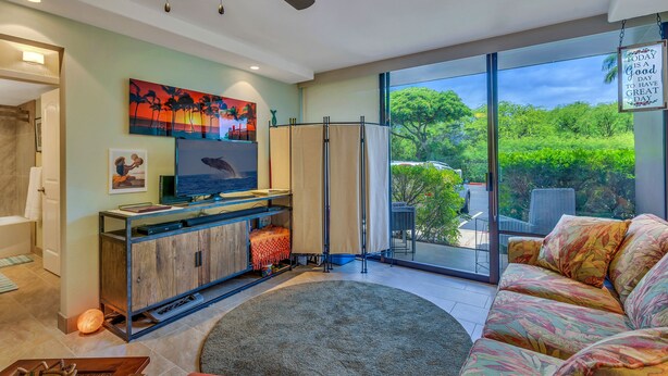 Een moderne woonkamer met een flatscreen televisie, een bank, een salontafel en een groot raam met uitzicht op groen.
