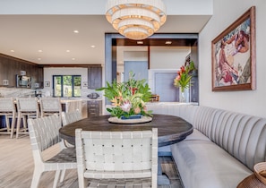 A modern kitchen with a central island, dining area with a round table and chairs, and a living area with a sofa and a painting.