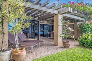 Un espacio exterior cubierto con un patio, una mesa y sillas, rodeado de plantas en macetas y un pequeño césped.