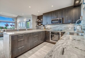 Una cocina moderna con armarios de madera oscura, una isla grande, electrodomésticos de acero inoxidable y vistas al exterior.