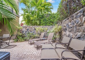 Un patio al aire libre con sillones de descanso y una mesa, rodeado por un muro de piedra y abundante vegetación.