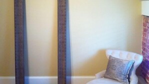 Una habitación con un espejo grande, una silla con cojín, suelo de madera y techo inclinado.
