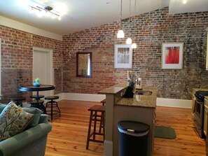 A kitchen with a brick wall, a small island with a sink, and a dining area with a table and chairs.