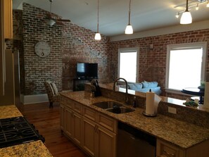 A kitchen with a brick wall, granite countertops, a built-in stove, a sink, and a television.