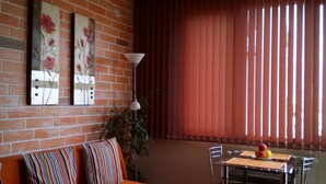 Une pièce avec un mur en briques, un canapé agrémenté de coussins colorés, une table à manger avec des chaises et une fenêtre avec des stores verticaux.