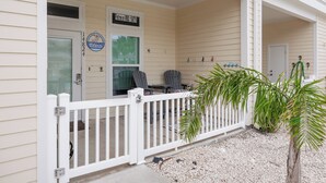 A house with a white porch, a welcome sign, a mailbox, and a small garden with a palm tree.