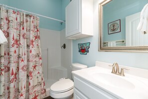 Une salle de bain avec des toilettes blanches, un lavabo avec un robinet doré, un rideau de douche aux motifs rouges et blancs, et un miroir fixé au mur.