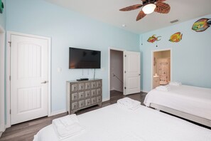 Une chambre avec deux lits, une télévision, un ventilateur de plafond et une commode.
