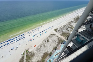 A beach with umbrellas and lounge chairs, a pool, and a view of the ocean.