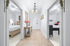 A hallway with a bed, bedside table, lamp, and a painting on the wall.