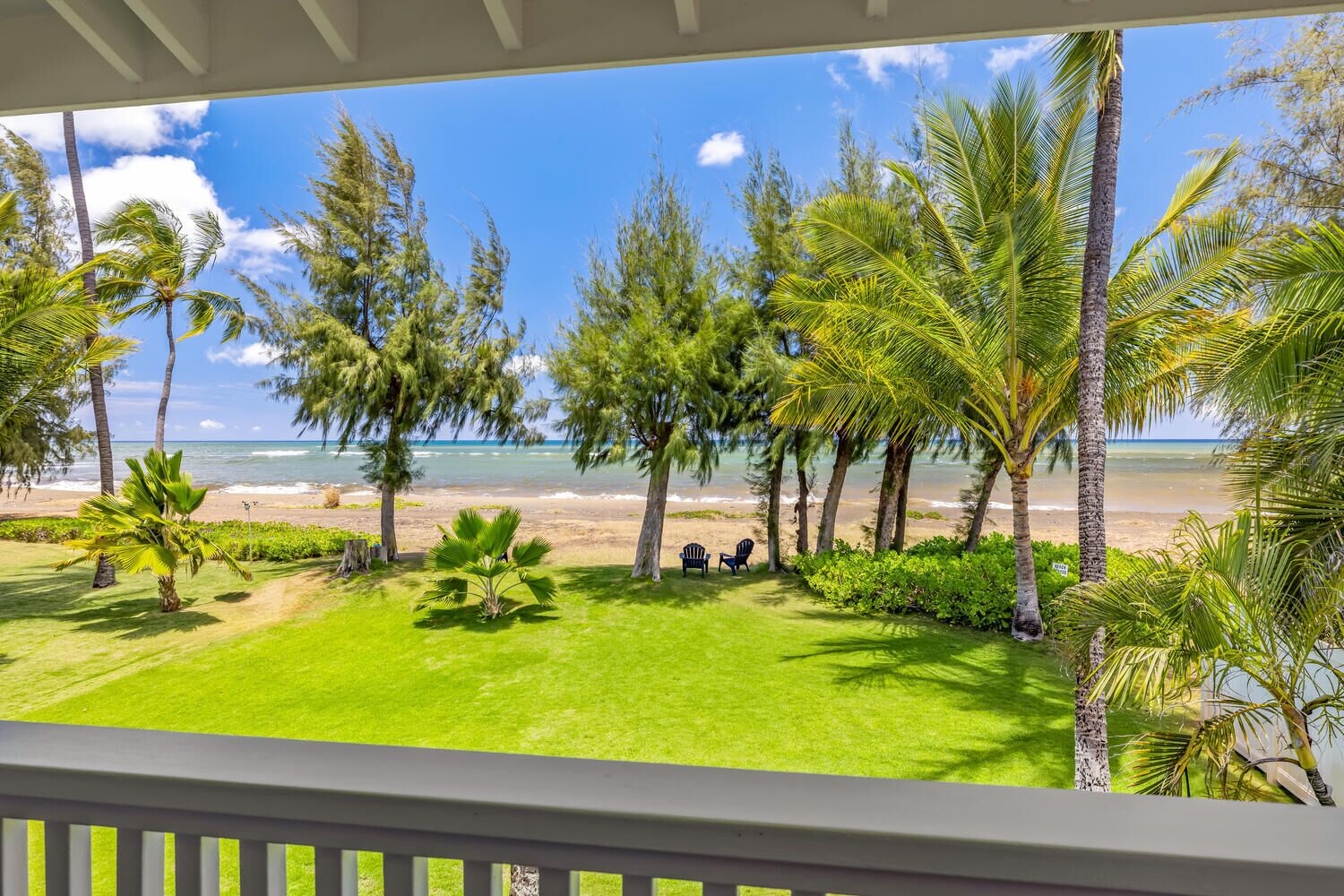 A view from a balcony overlooking a beach with palm trees and a clear sky.