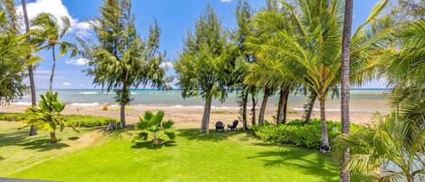 A view from a balcony overlooking a beach with palm trees and a clear sky.