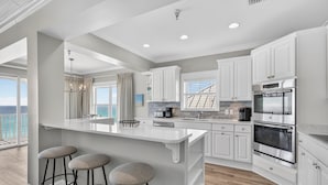 A modern kitchen with white cabinetry, a large island with stools, and a view of the ocean.