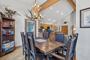 A dining area with a wooden table and chairs, a chandelier, and a kitchen in the background. - Beautiful Mountain Townhome with Hot Tub, Convenient Location! HL305 (Breckenridge)