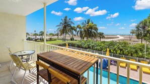 Un balcón con mesa y sillas de madera, con vista a una piscina y palmeras.
