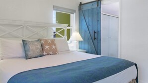 Un dormitorio con una cama, almohadas, una mesita de noche, una lámpara y un armario azul.