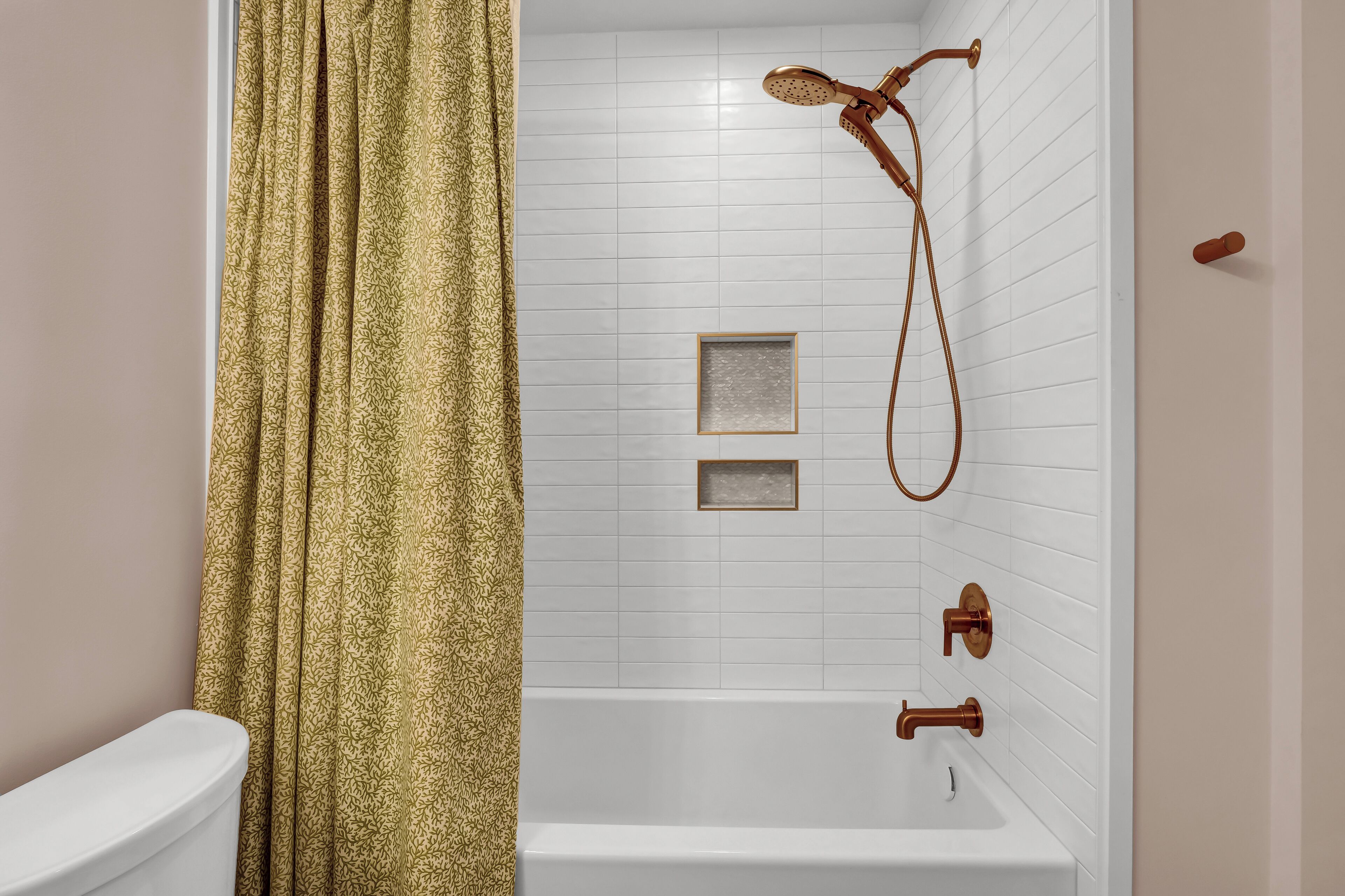 A bathroom with a white bathtub, a showerhead, and a toilet.