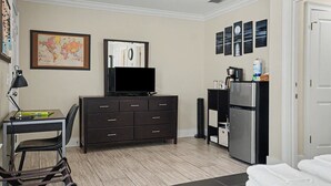 A hotel room with a desk, dresser, television, refrigerator, and a bed. - Modern Suite for the Traveling Professional by Lucky Savannah (Savannah)