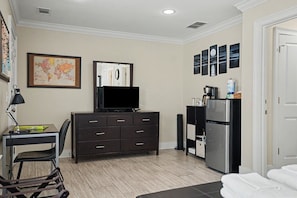 A hotel room with a desk, dresser, television, refrigerator, and a bed.