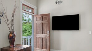 A room with a wooden door, a television mounted on the wall, and a vase with branches on a table. - Modern Suite for the Traveling Professional by Lucky Savannah (Savannah)