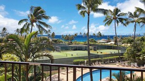 Ett poolområde med en tennisbana, palmer och utsikt över havet.