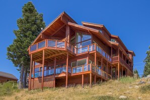 A multi-story wooden cabin with large windows and balconies, surrounded by trees and a grassy landscape. - Big Sky - Lakeview - TLUXP (Truckee)