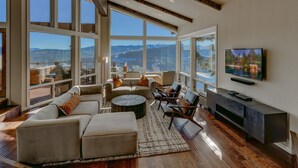 A spacious living room with large windows, a comfortable seating area, and a flat-screen TV mounted on the wall. - Big Sky - Lakeview - TLUXP (Truckee)