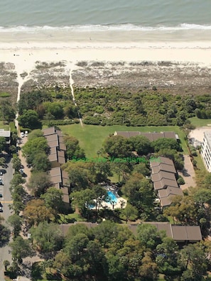 Vue aérienne d’une propriété située sur la côte, avec plusieurs bâtiments, une piscine et une plage en arrière-plan.
