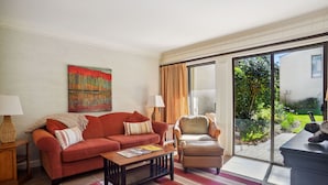 A living room with a sofa, armchair, coffee table, and a large window with curtains.