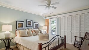A bedroom with a bed, two bedside tables, a ceiling fan, a window with curtains, and a closet with louvered doors.
