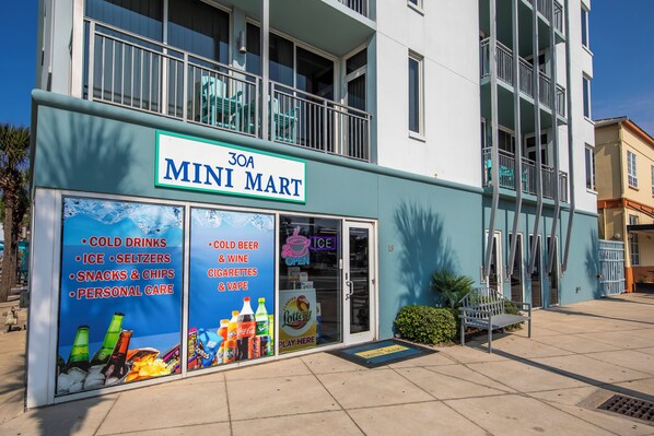 A building with a sign for 'Mini Mart' on the ground floor, featuring a list of items like cold drinks, ice, snacks, and personal care. - Idle Hours - Pet Friendly! Gulf Front in Dune Allen Beach (Santa Rosa Beach)