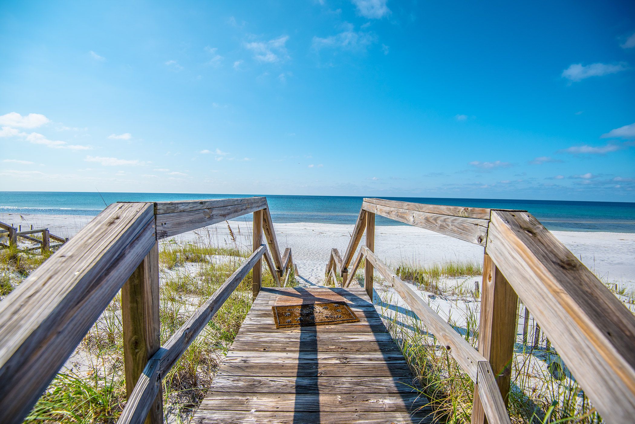 A wooden boardwalk leading to a beach with clear skies.