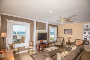 A living room with a large window, a ceiling fan, and a television. - Idle Hours - Pet Friendly! Gulf Front in Dune Allen Beach (Santa Rosa Beach)