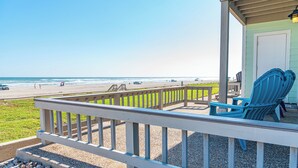 A beach view from a porch with a railing, a door, and two blue Adirondack chairs.