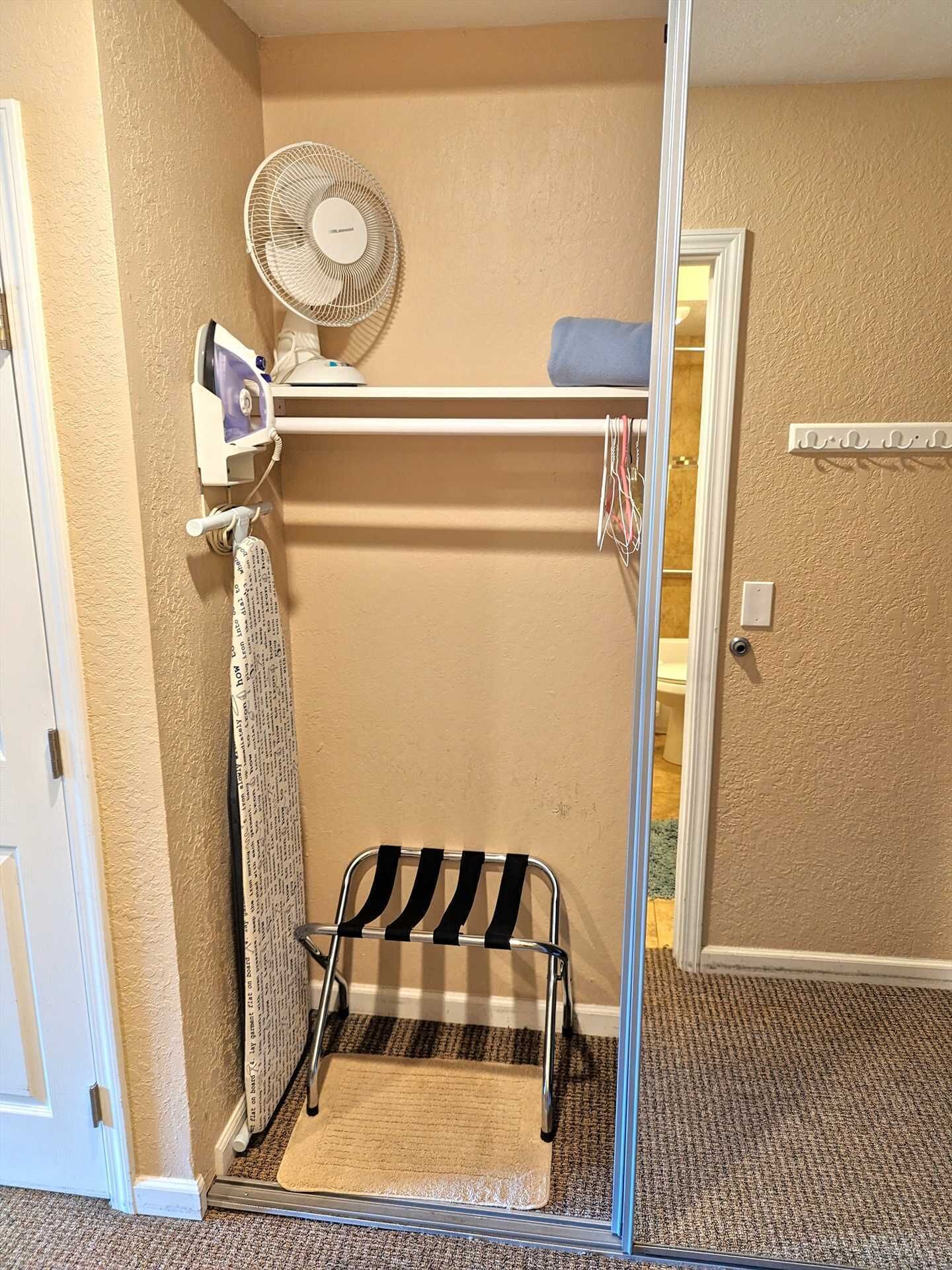 A small room with a fan, ironing board, and a small stool.