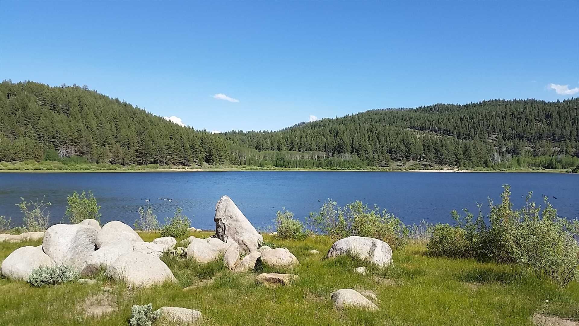 Un lago rodeado de colinas boscosas y grandes rocas en primer plano.