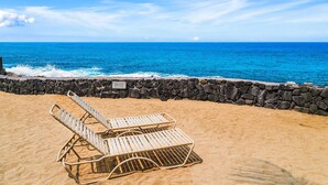 A beach with two sun loungers and a stone wall.
