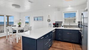 A modern kitchen with a large island, dark cabinetry, and a view to the outside.