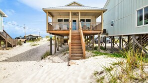 A beach house with a wooden staircase leading to a covered porch.