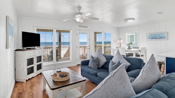 A living room with a blue sofa, a television on a cabinet, and a ceiling fan.