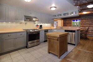 A kitchen with grey cabinets, stainless steel appliances, a wooden island, and a wooden wall.