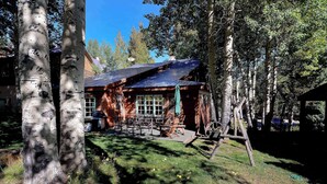 A rustic cabin with a metal roof, surrounded by trees and a grassy area with outdoor seating. - Gothic Charmer,Charming home on the West End of CB (Crested Butte)
