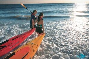 Deux kayaks sont sur la plage, et des personnes se tiennent à proximité.