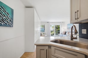 Una cocina moderna con una isla grande, muebles blancos y vistas a un balcón.