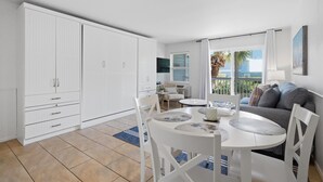 A modern kitchen with white cabinetry, a dining table with chairs, and a view of the outdoors. - "Inlet Sands 204" | 1 min. walk to beach | Community Pool | Bike to Rosemary (Inlet Beach)