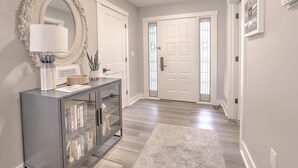 Un couloir avec une console grise, un grand miroir et une porte dotée d’un panneau de verre.