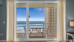 A balcony with a table and chairs, overlooking a beach and ocean.