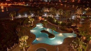 Ein Poolbereich eines Resorts mit einem geschwungenen Pool, umgeben von Palmen und Liegestühlen.